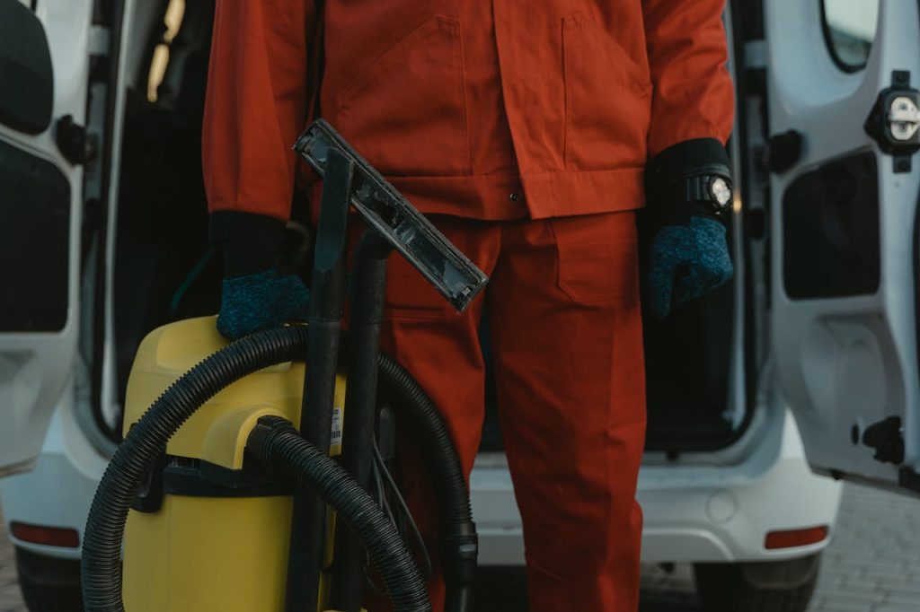 Mastering the First Impression: Your intriguing post title goes here A professional cleaner in a red uniform holding a vacuum near a van, ready for service.